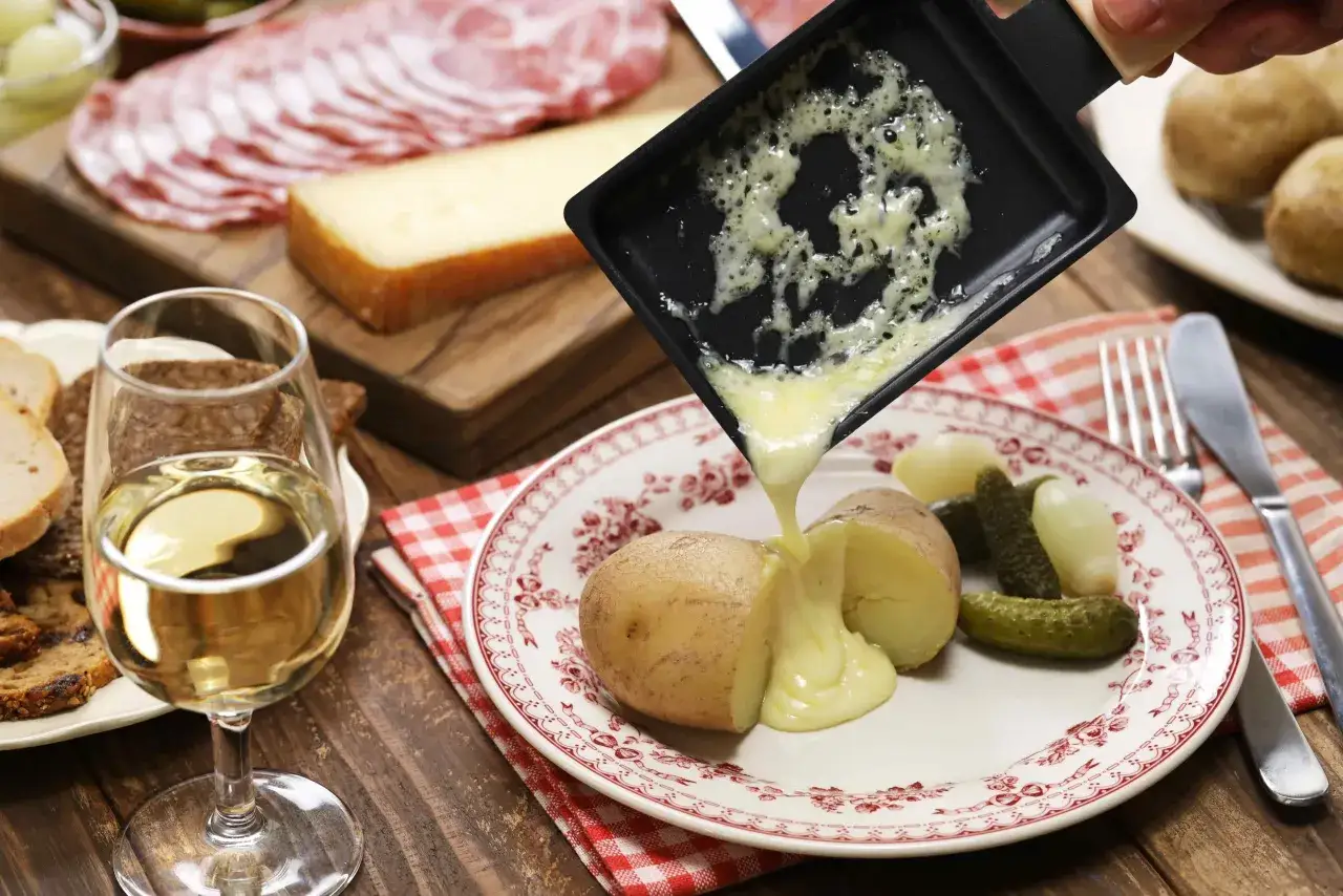Un verre de Chablis accompagne une raclette fondante versée sur des pommes de terre et des cornichons. Un festin savoureux !
