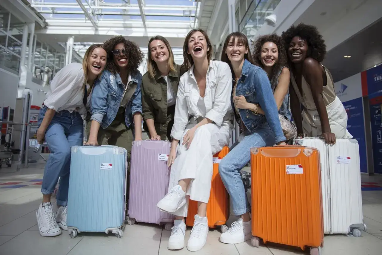 Groupe de femmes joyeuses &agrave; l'a&eacute;roport, pr&ecirc;tes pour leur EVJF en France. Valises color&eacute;es et sourires &eacute;clatants.