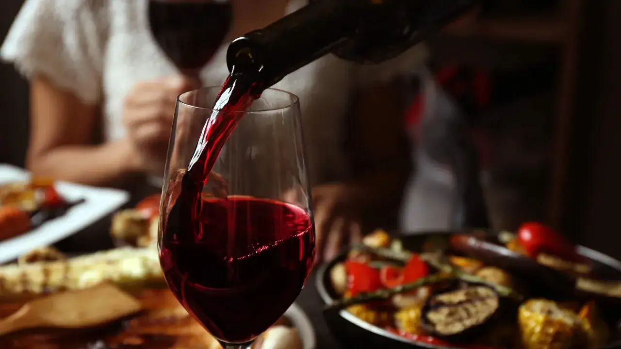 Un verre de vin rouge est versé, prêt à accompagner une délicieuse entrecôte et des légumes grillés.