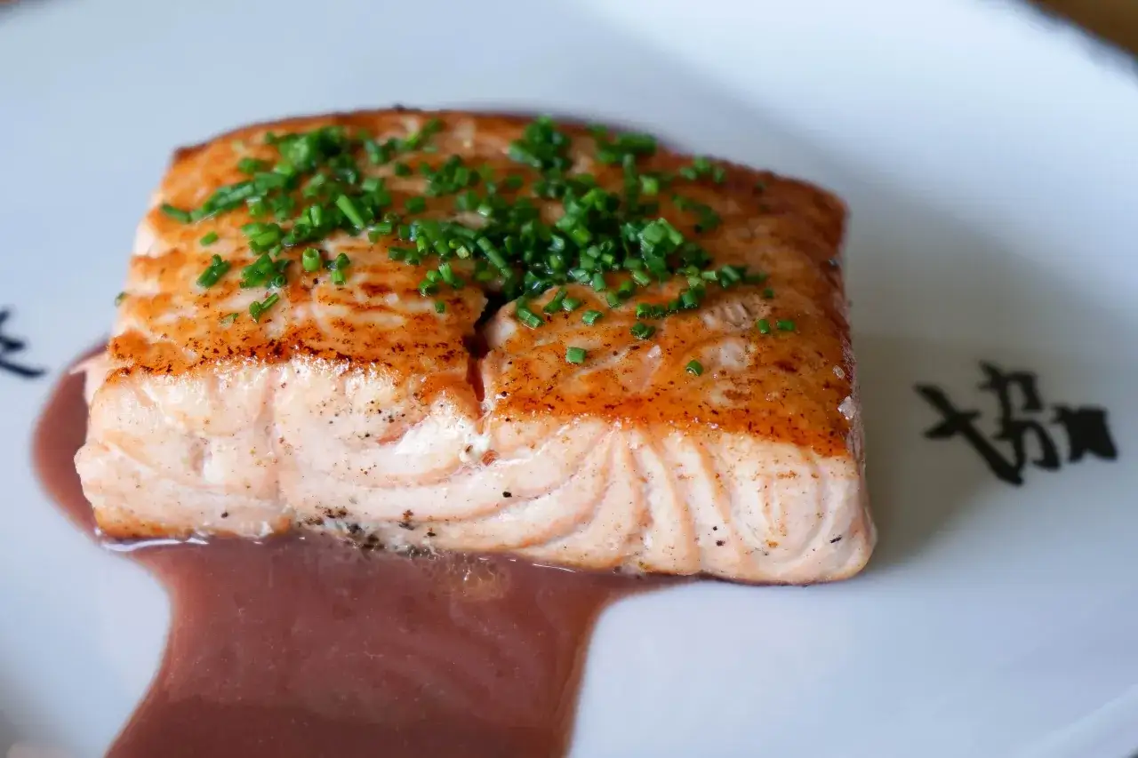 Filet de saumon poêlé, garni de ciboulette, baignant dans une sauce rouge. Un plat qui invite à se demander quel vin rouge avec du saumon.