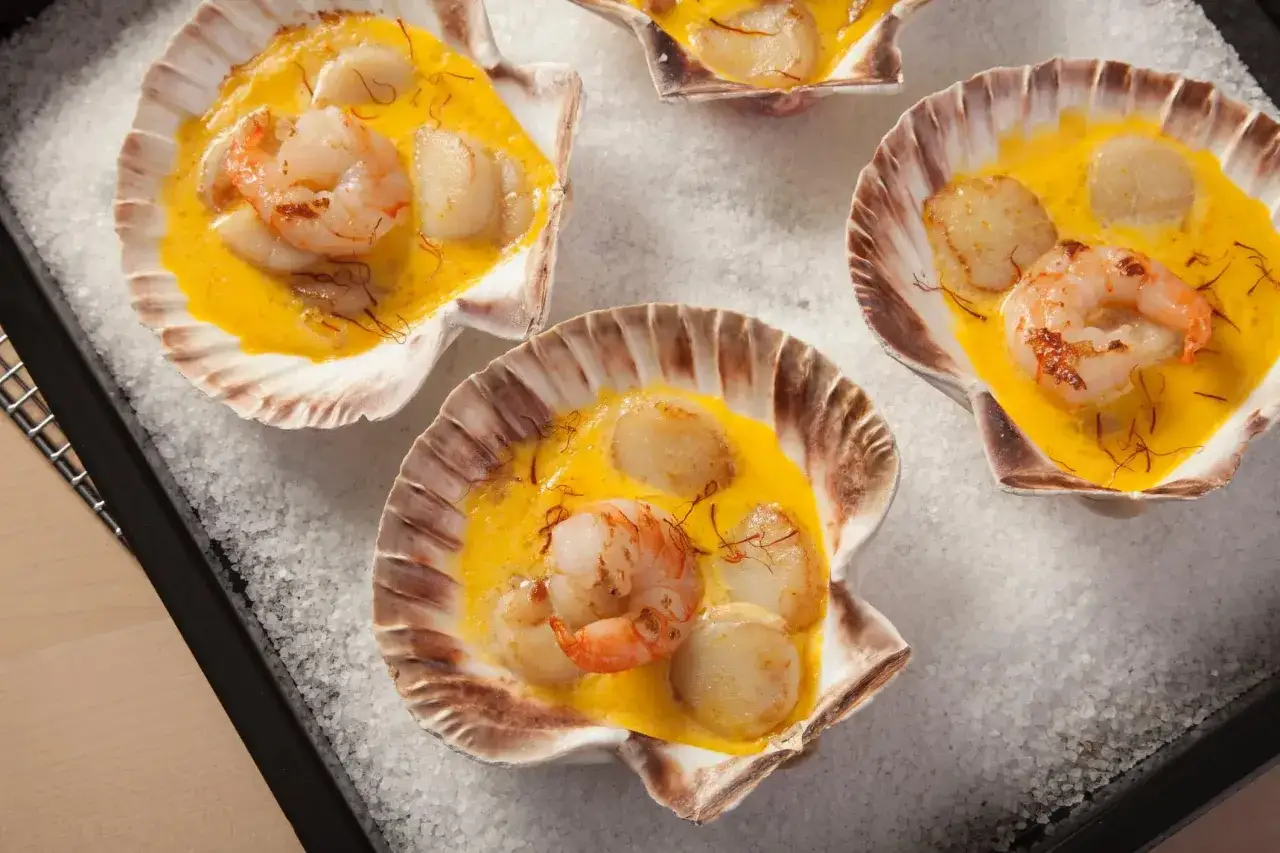 Coquilles Saint-Jacques au safran et vin blanc, garnies d'une crevette, baignant dans une sauce onctueuse. Un délice visuel et gustatif.
