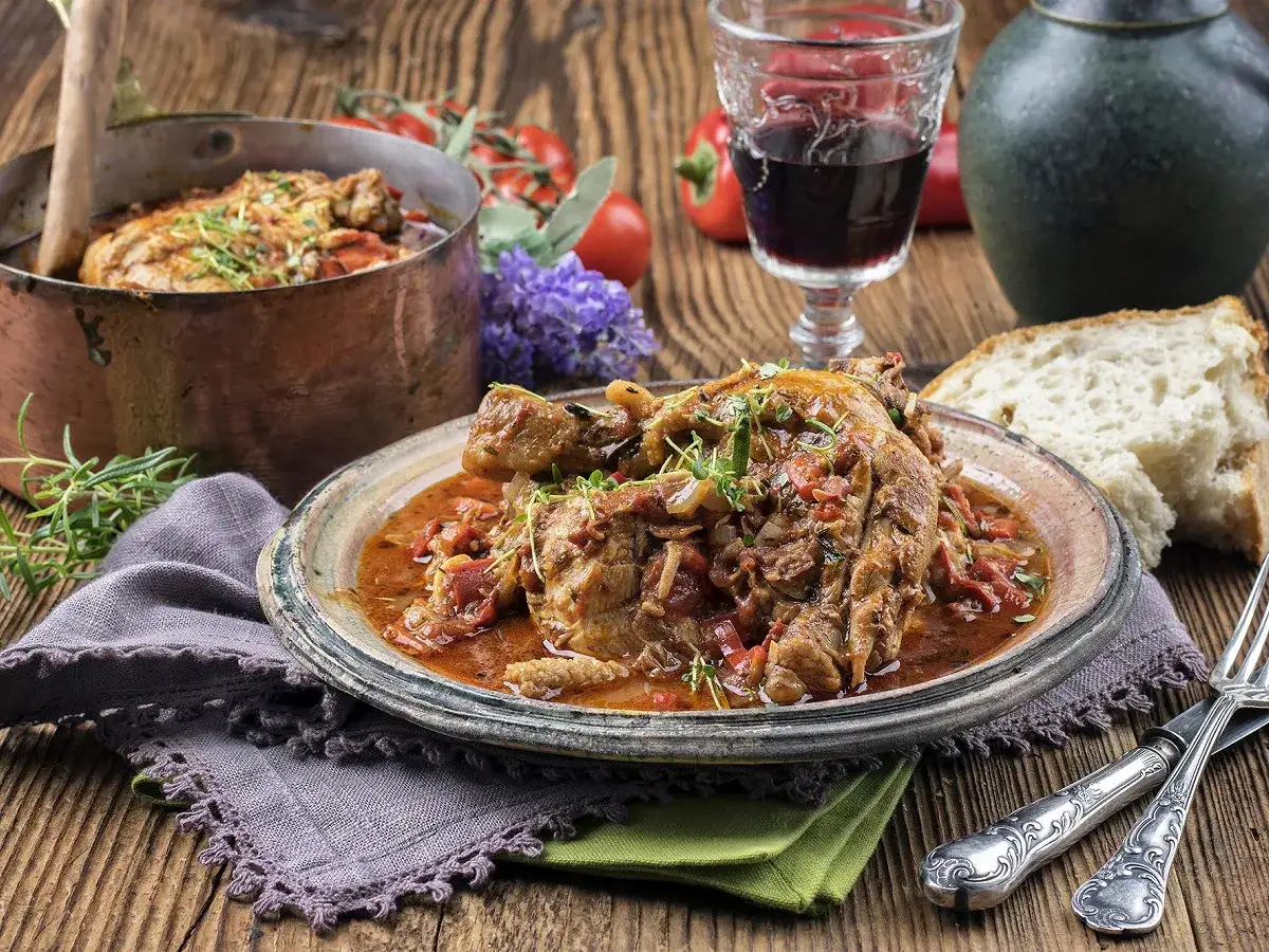 Un plat appétissant de vin avec poulet basquaise, garni d'herbes fraîches, servi avec du pain croustillant et un verre de vin rouge.