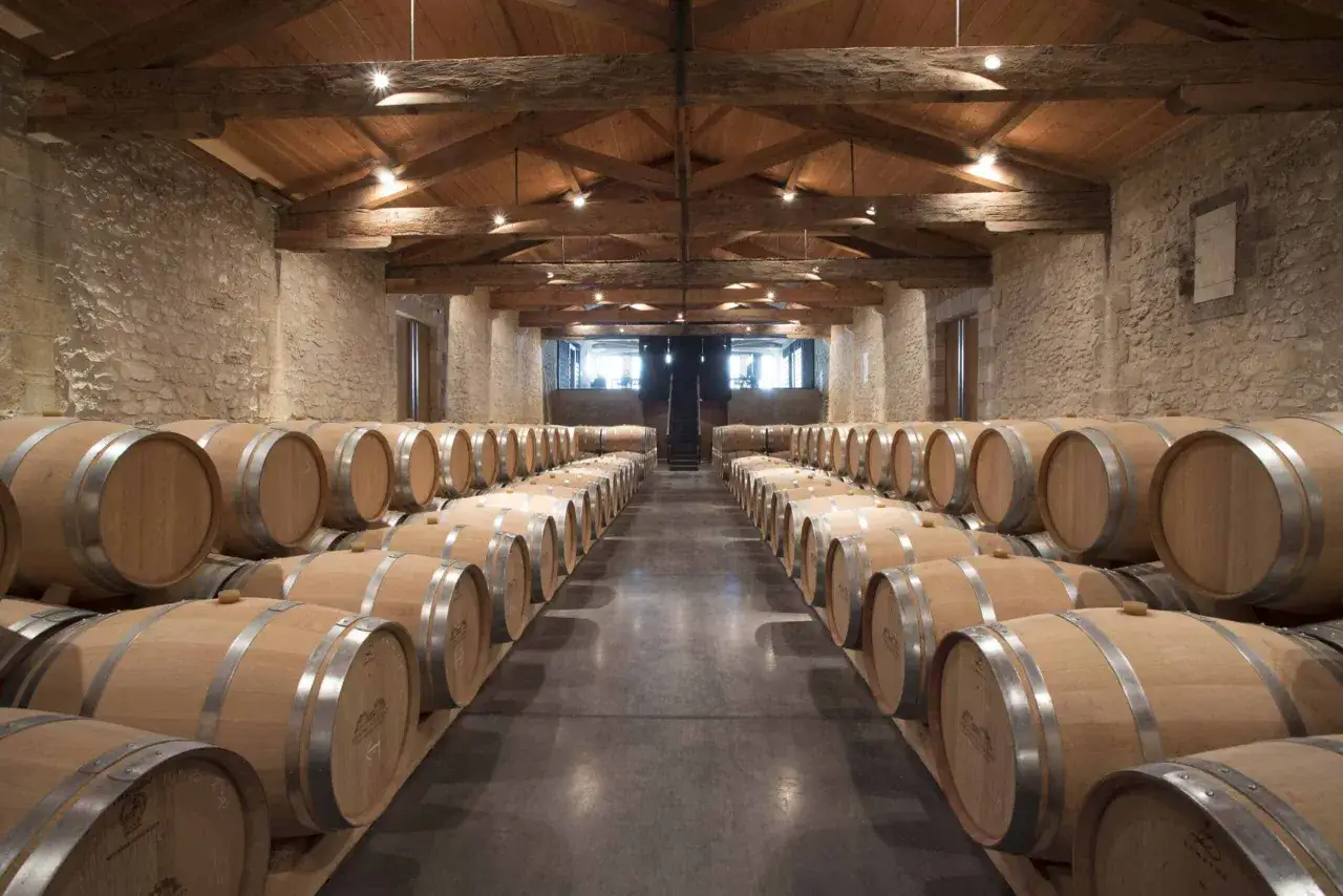 Cave voûtée en pierre avec des rangées de fûts en bois, prêts à vieillir les meilleures années Saint-Emilion Grand Cru.