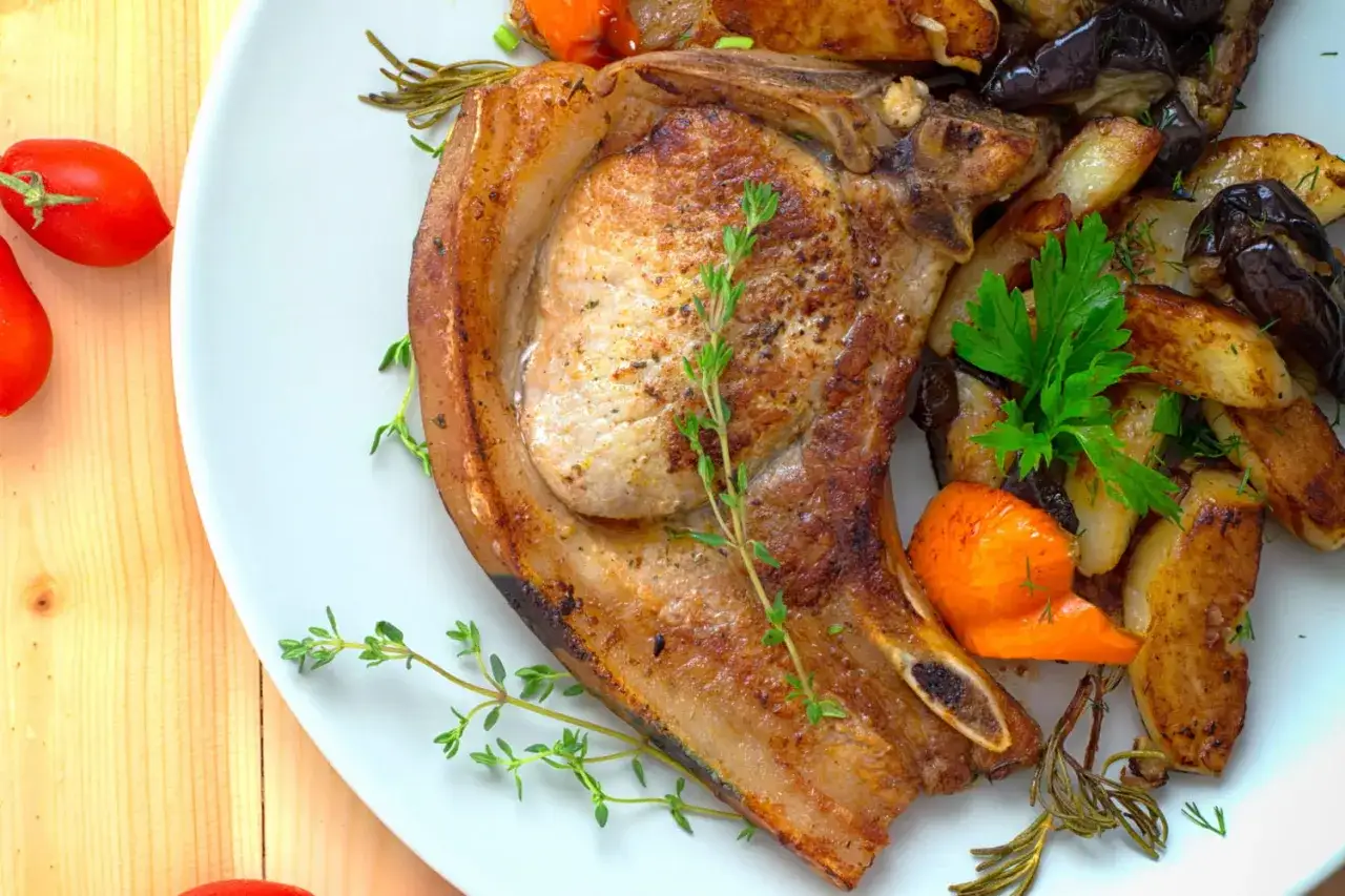 Une côte de porc rosé parfaitement grillée, accompagnée de légumes rôtis et d'herbes fraîches. Un délice visuel et gustatif.