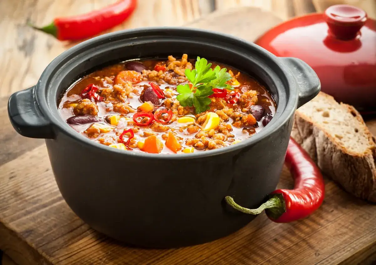 Un chili savoureux mijote dans une cocotte en fonte, parfaite pour aller au four. Accompagn&eacute; de pain et de piments rouges.