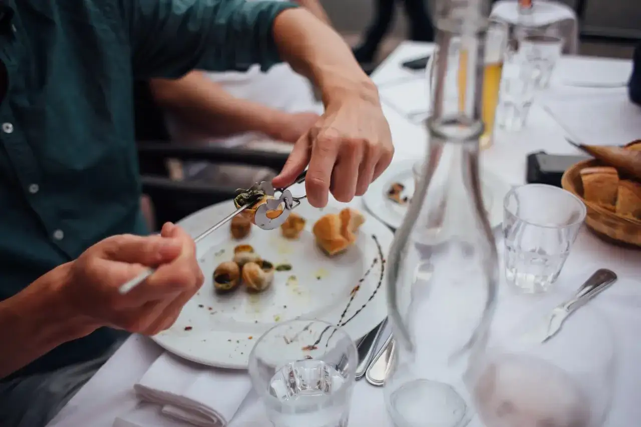 Un homme déguste des escargots, un plat qui invite à se demander quel vin avec les escargots. Une belle table dressée pour un repas convivial.