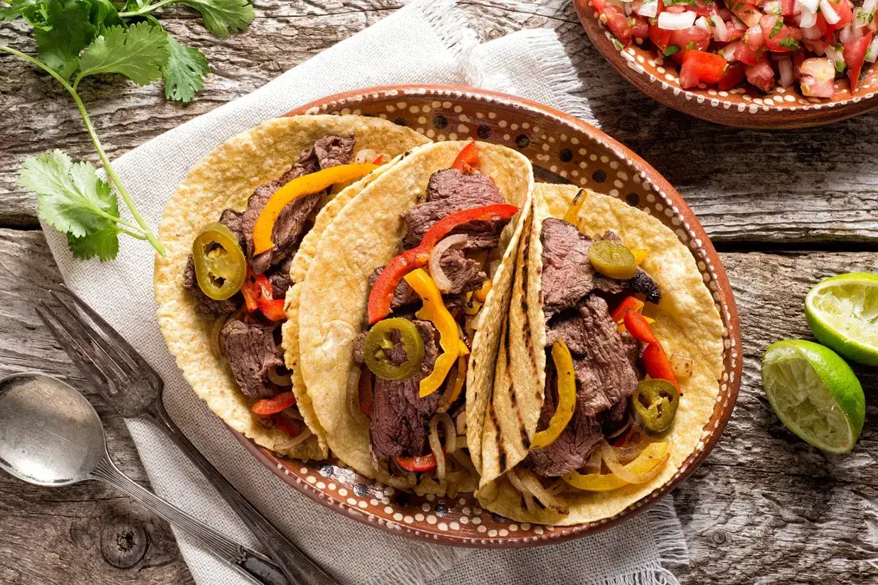 Trois fajitas garnies de bœuf, poivrons et jalapeños, prêtes à être dégustées avec un verre de vin.