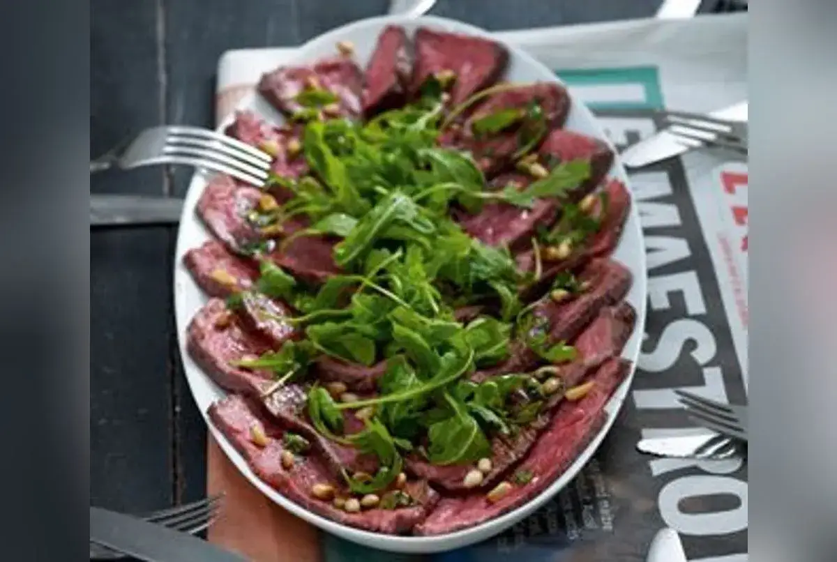 Un rôti de boeuf froid pour 20 personnes, finement tranché, garni de roquette fraîche et de pignons de pin. Un plat élégant pour un grand repas.