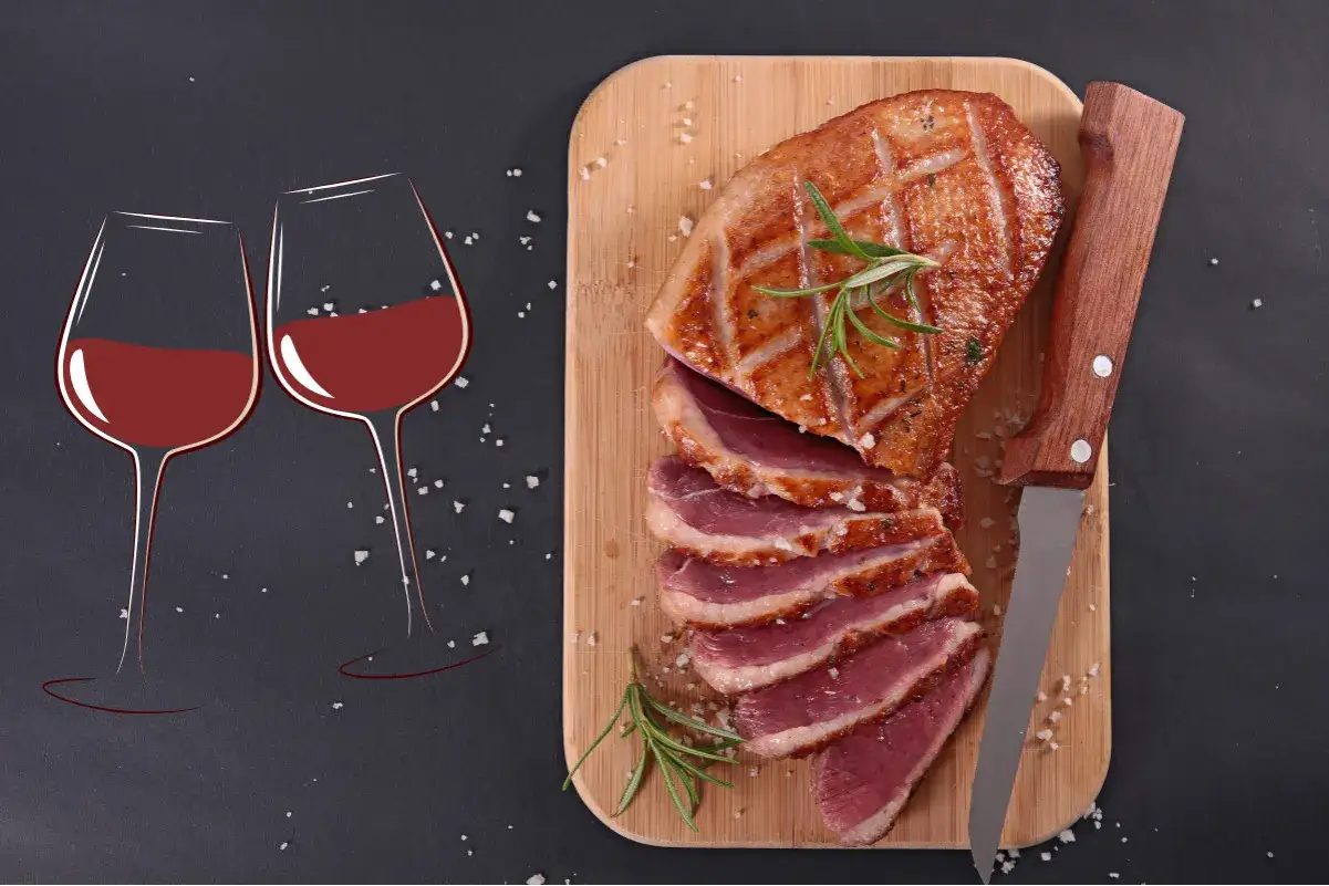 Un canard rôti tranché sur une planche, accompagné de deux verres de vin rouge. Quel vin rouge avec du canard ? Un accord parfait pour un repas savoureux.