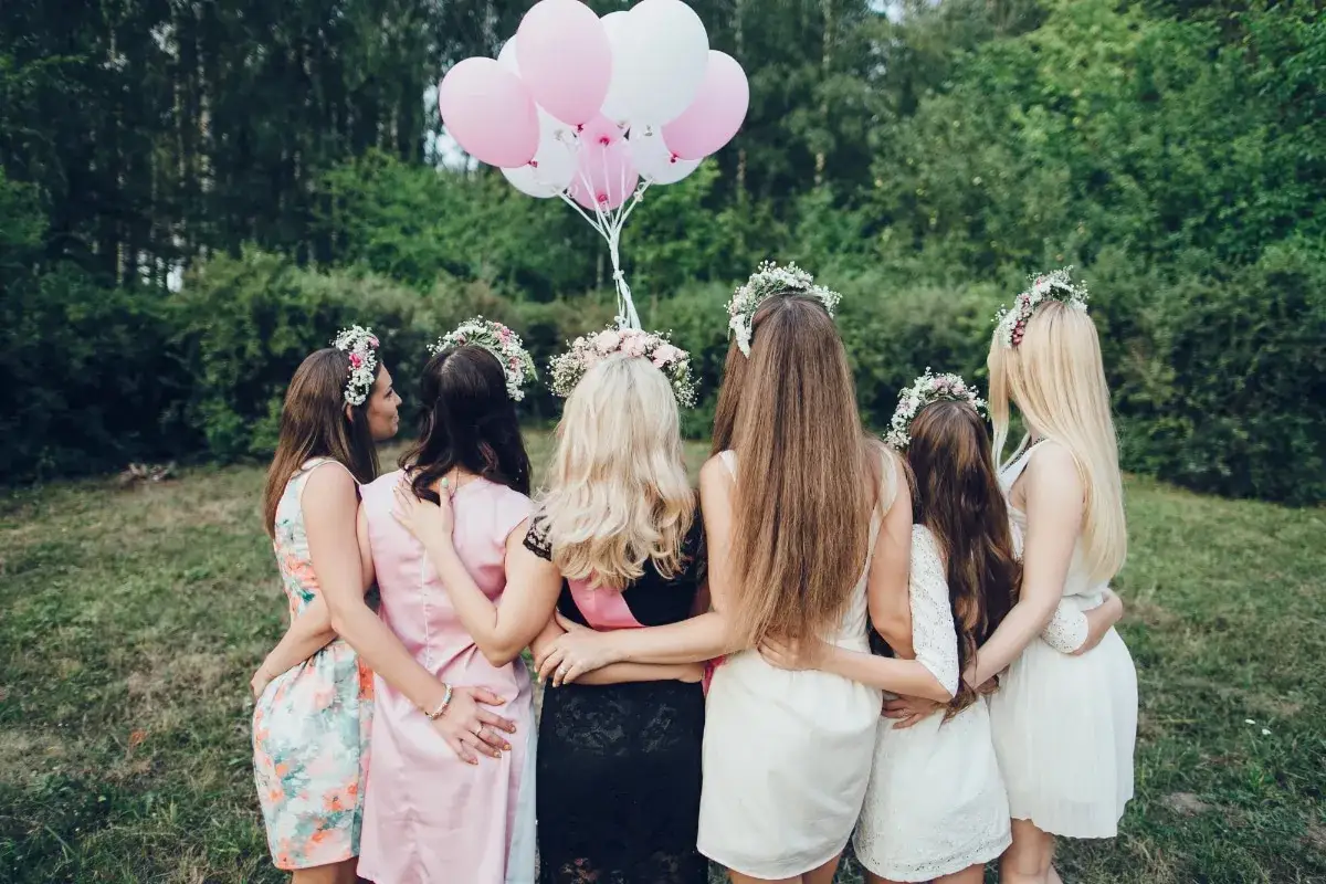 Groupe de femmes en robes d'&eacute;t&eacute; et couronnes de fleurs, bras autour des &eacute;paules, avec des ballons roses et blancs. Id&eacute;al pour des jeux EVJF &agrave; imprimer gratuit.