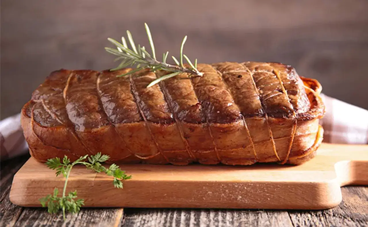 Un rôti de veau savoureux, ficelé et garni de romarin, prêt à être dégusté avec un bon vin.