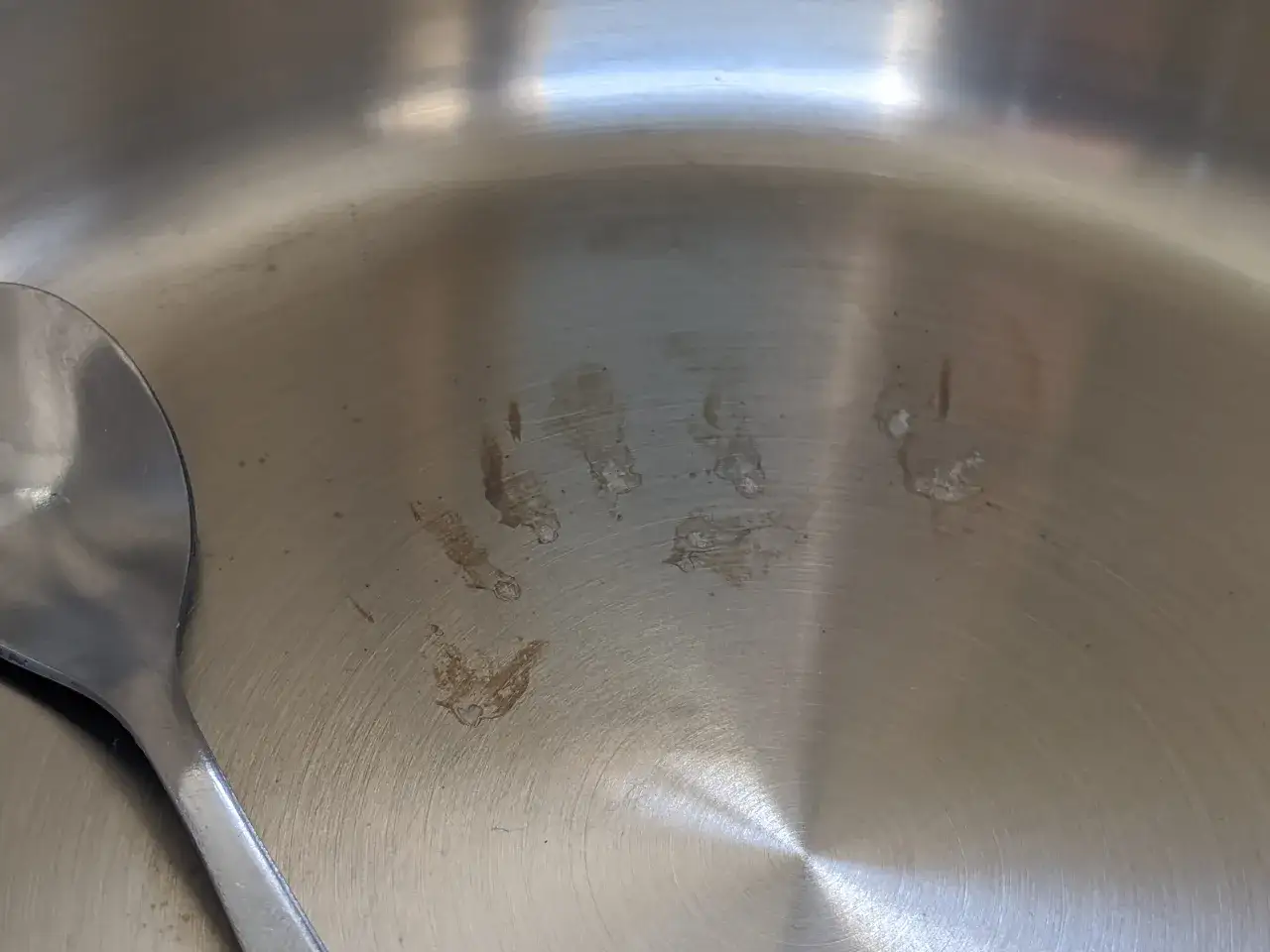 Une cuill&egrave;re repose dans une casserole en inox, marqu&eacute;e de quelques taches bleues et de r&eacute;sidus de cuisson.