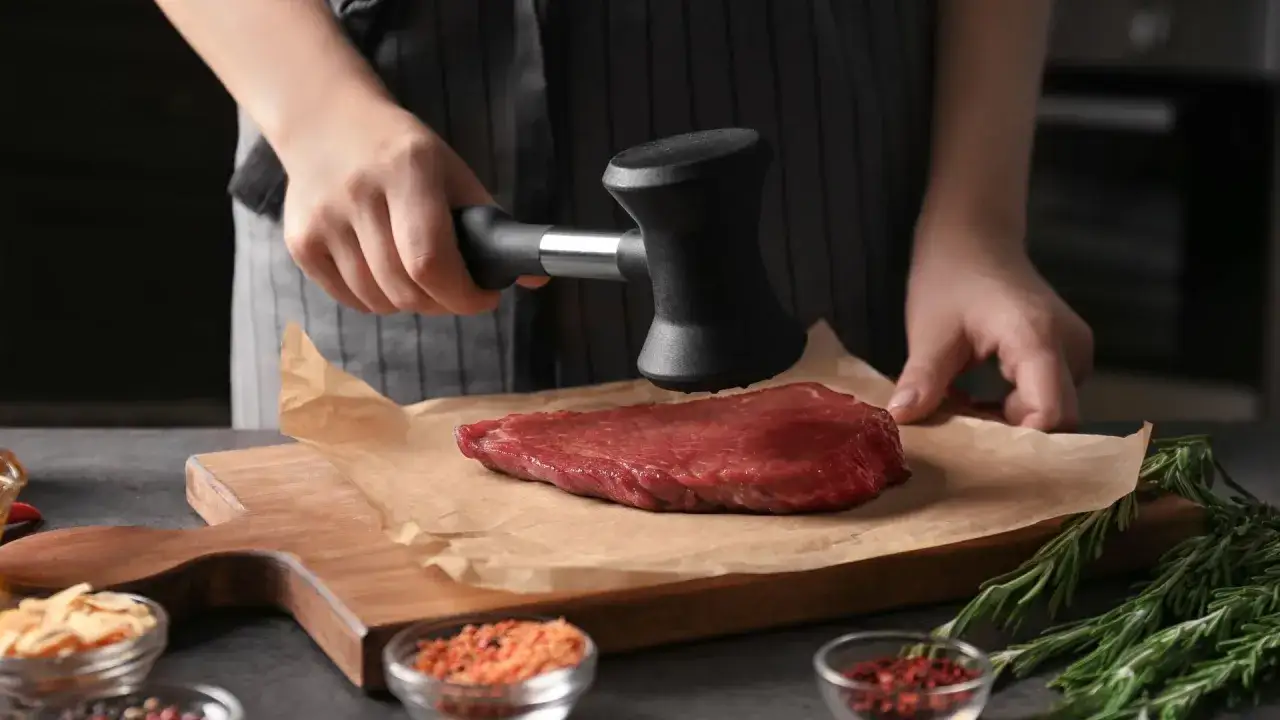 Une main utilise un attendrisseur pour aplatir un steak. C'est une &eacute;tape cl&eacute; pour comprendre pourquoi taper la viande rend les plats plus tendres et savoureux.