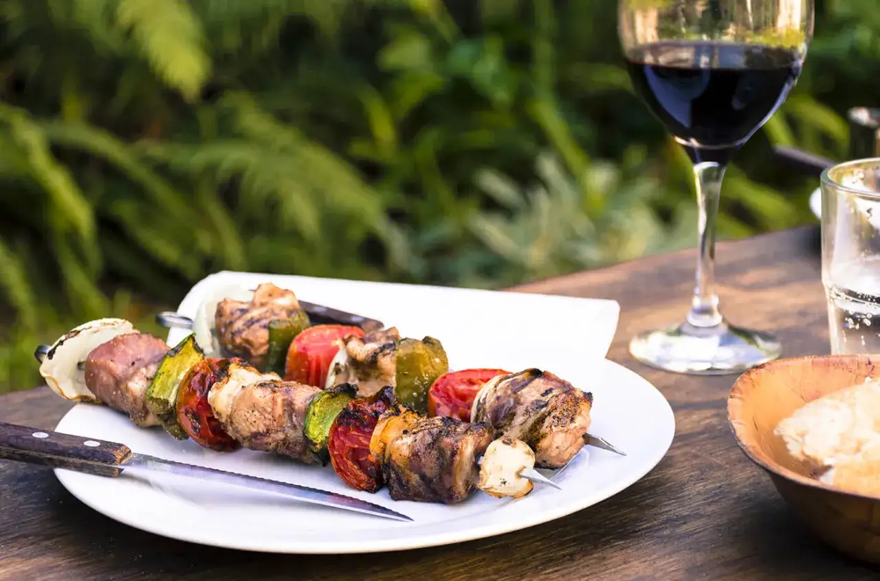 Brochettes de viande et légumes grillés, accompagnées d'un verre de vin rouge. Parfait pour un barbecue estival.