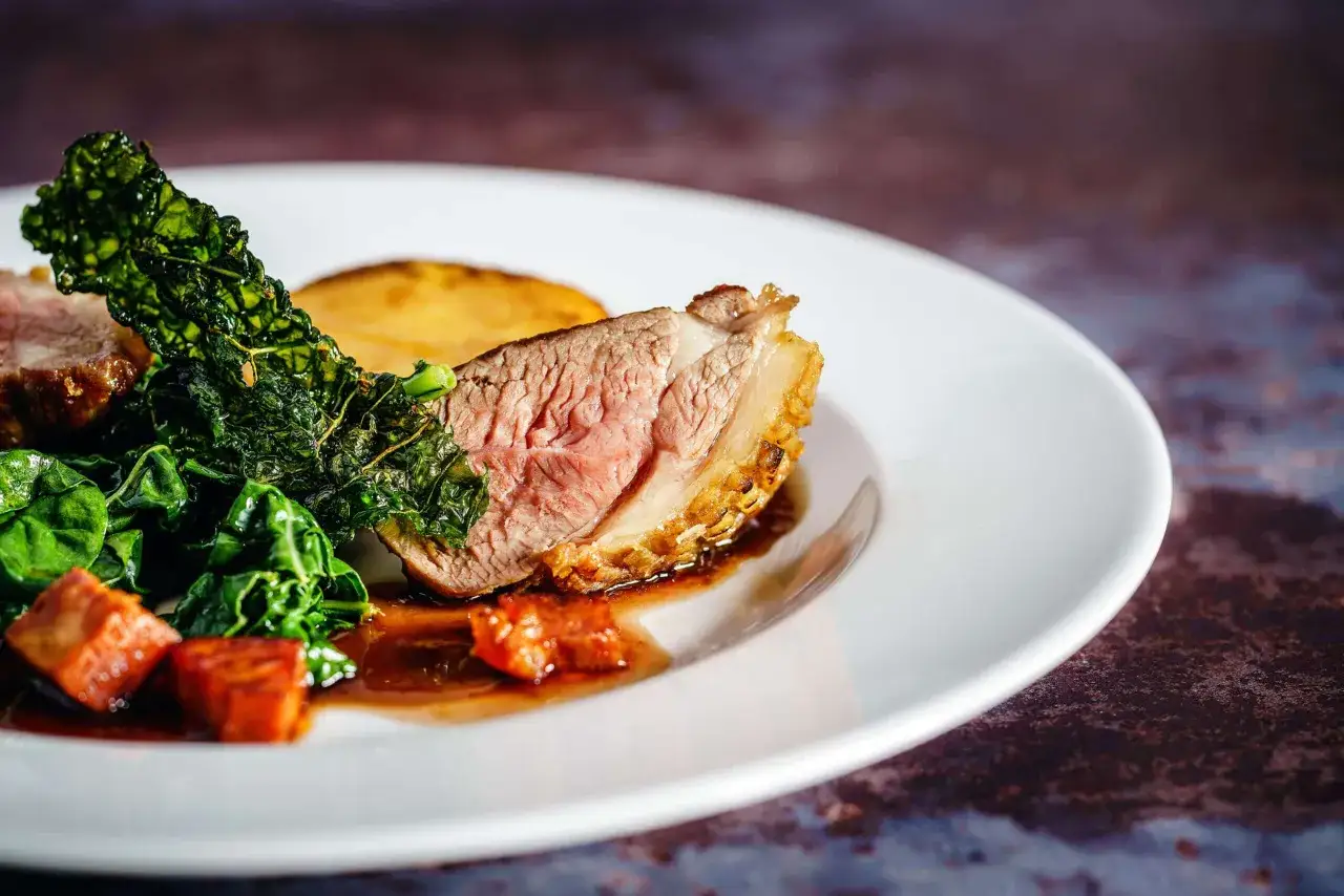 Un plat de vin avec agneau, accompagné de légumes verts et d'une tranche de pomme de terre rôtie.