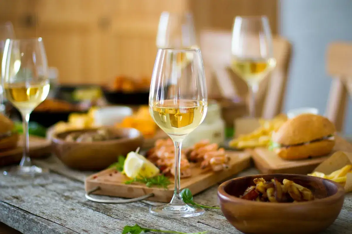 Verre de vin blanc, crevettes, frites et un burger sur une table en bois. Une tranche de citron apporte une touche de fraîcheur.