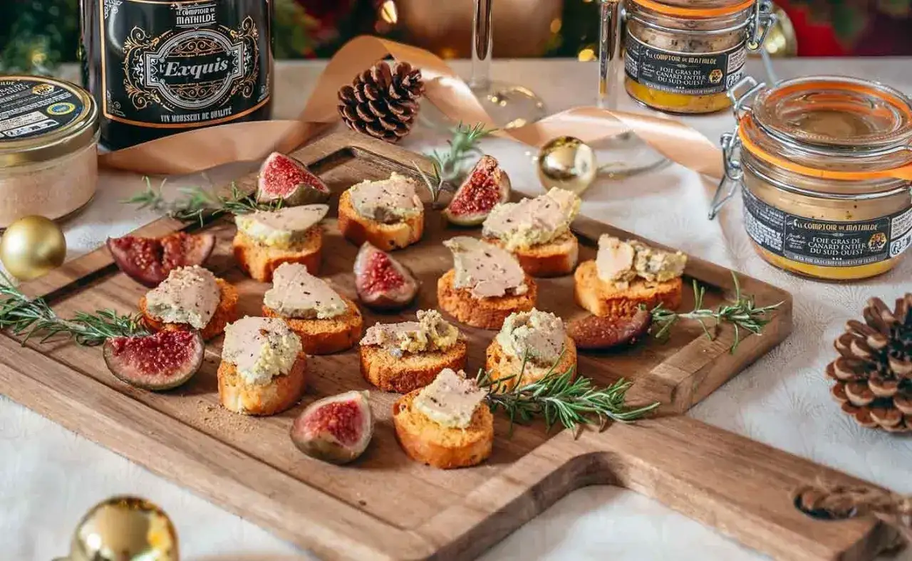 Toasts de foie gras, figues et romarin sur planche en bois. Une bouteille d'Exquis et des bocaux de foie gras suggèrent quoi boire avec du foie gras pour un repas festif.