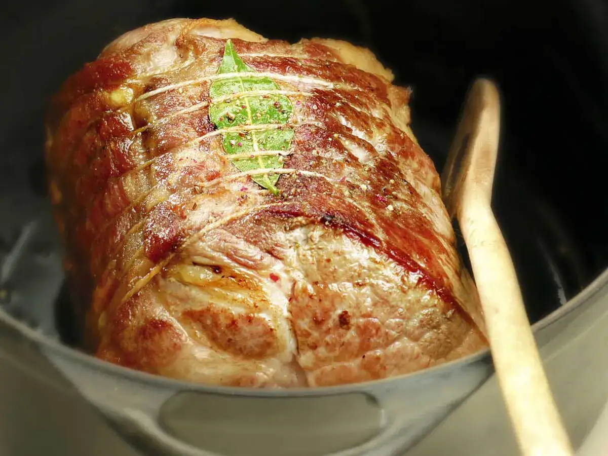 Gros plan sur un rôti de porc au vin blanc, doré et savoureux, prêt à être dégusté. Une feuille de laurier orne sa surface.