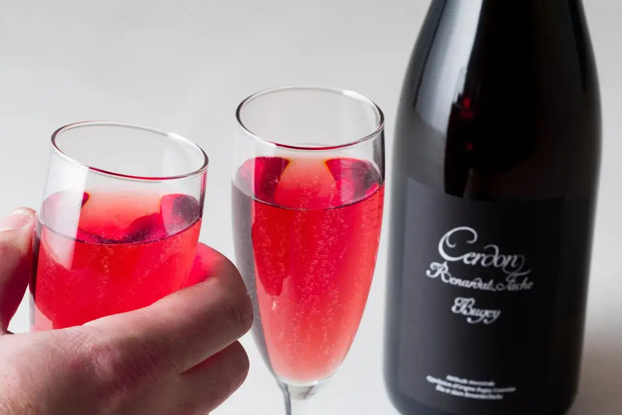 Deux verres de Cerdon blanc pétillant, d'une belle couleur rosée, sont prêts à être dégustés à côté de la bouteille.