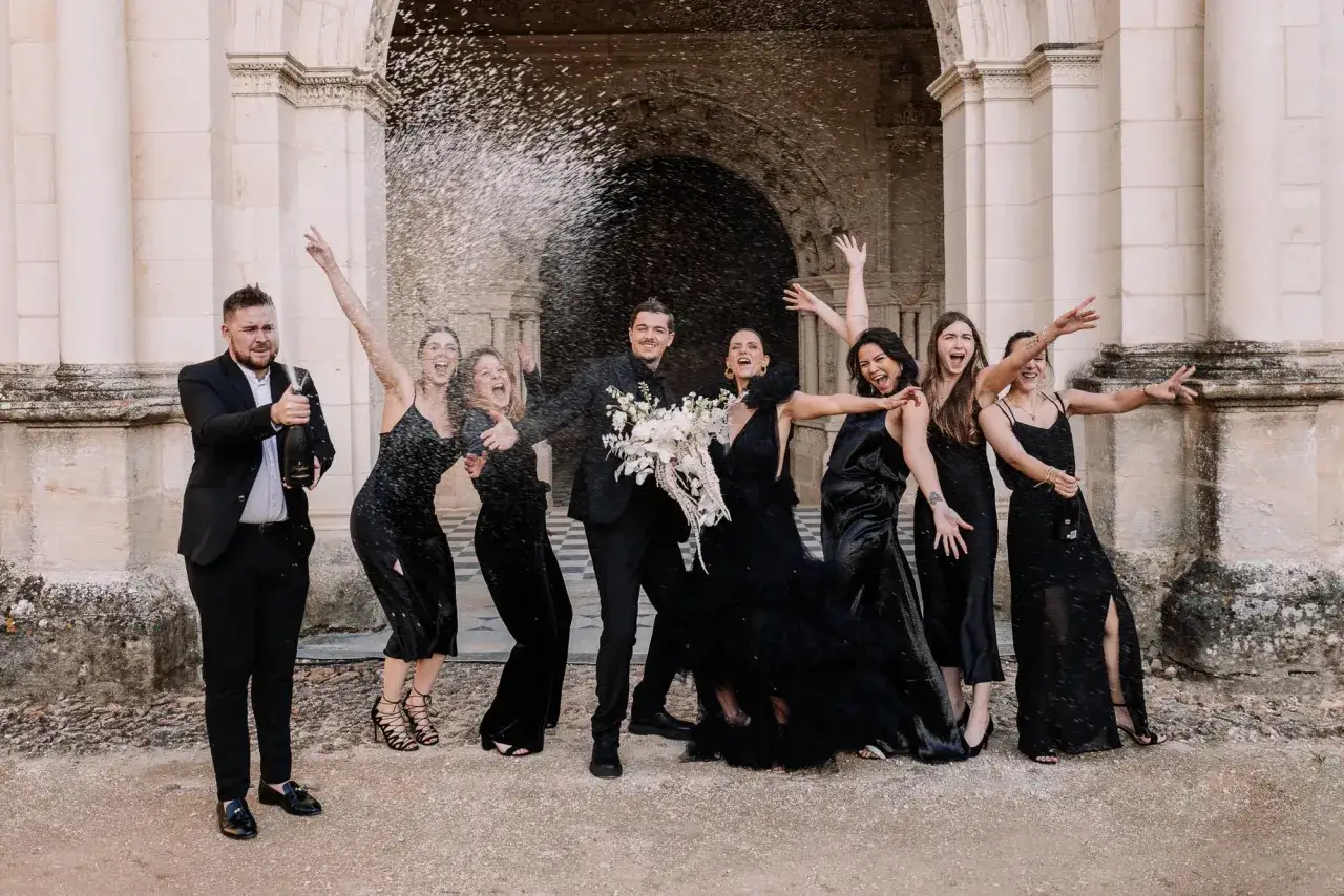 Un groupe joyeux c&eacute;l&egrave;bre un mariage noir et blanc, le mari&eacute; ouvrant une bouteille de champagne tandis que les demoiselles d'honneur crient de joie.
