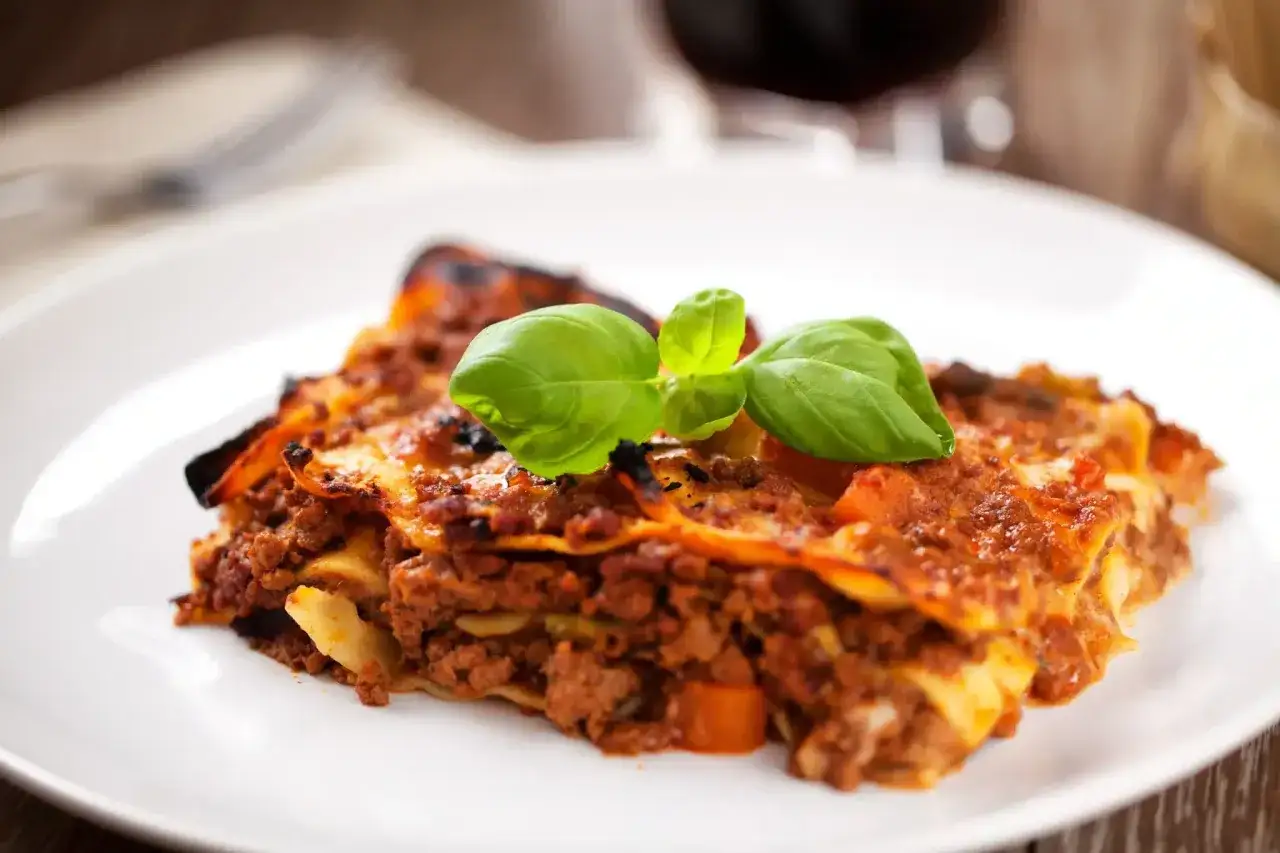 Une part de lasagnes à la bolognaise, garnie de basilic frais. Un plat réconfortant, parfait avec un verre de vin rouge. Quel vin avec des lasagnes ?