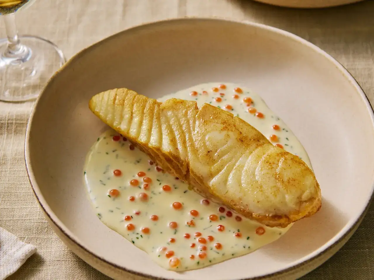 Un délicieux poisson à la crème et vin blanc, parsemé de perles orangées et d'herbes fraîches, servi dans une assiette creuse.