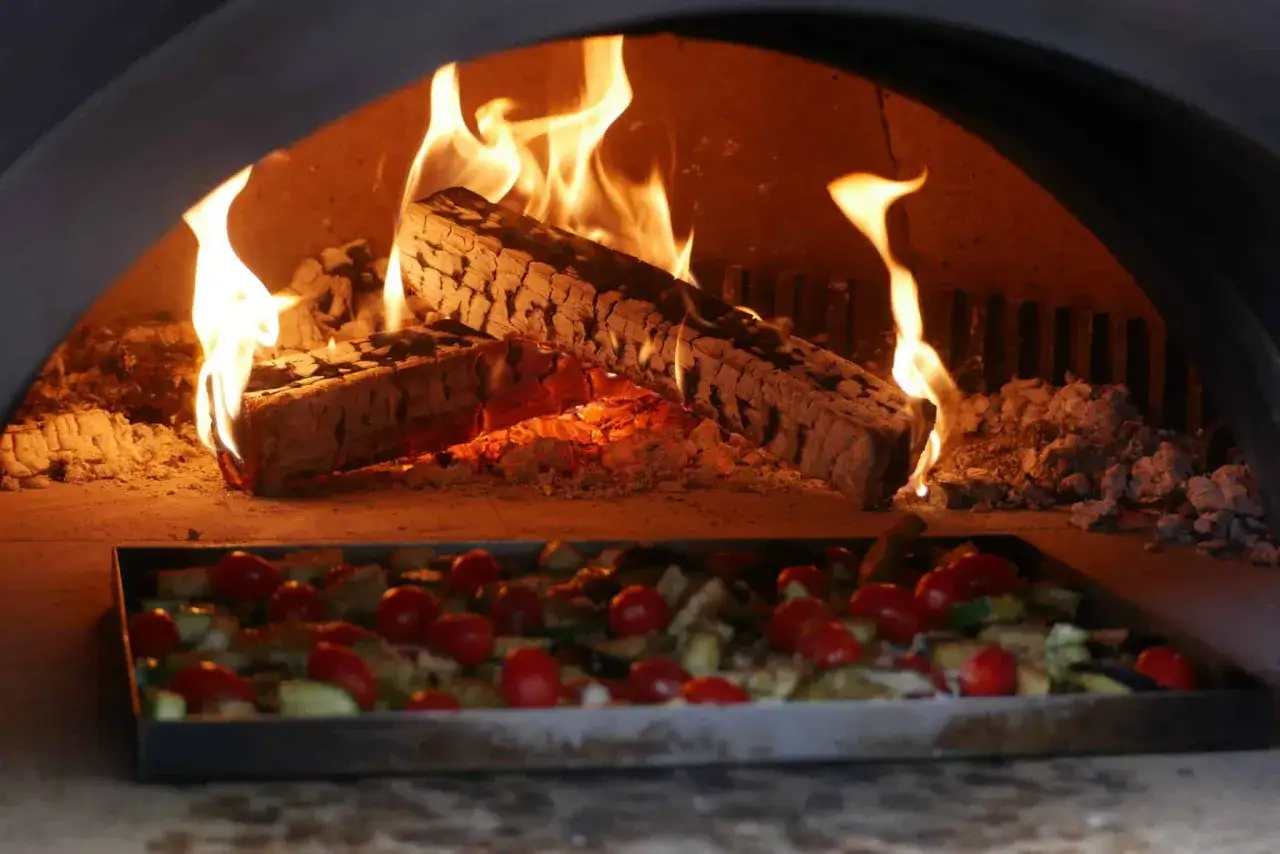 Un plat pour four à bois, rempli de légumes et de tomates, est prêt à être cuit dans la chaleur des flammes vives.