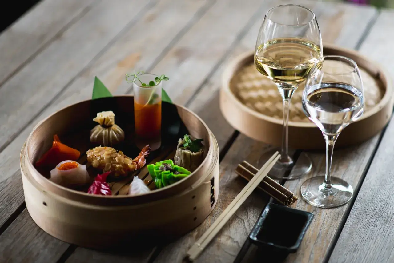 Assortiment de dim sum colorés dans un panier vapeur, avec deux verres de vin blanc et de l'eau. Parfait pour savoir que boire avec une fondue chinoise.