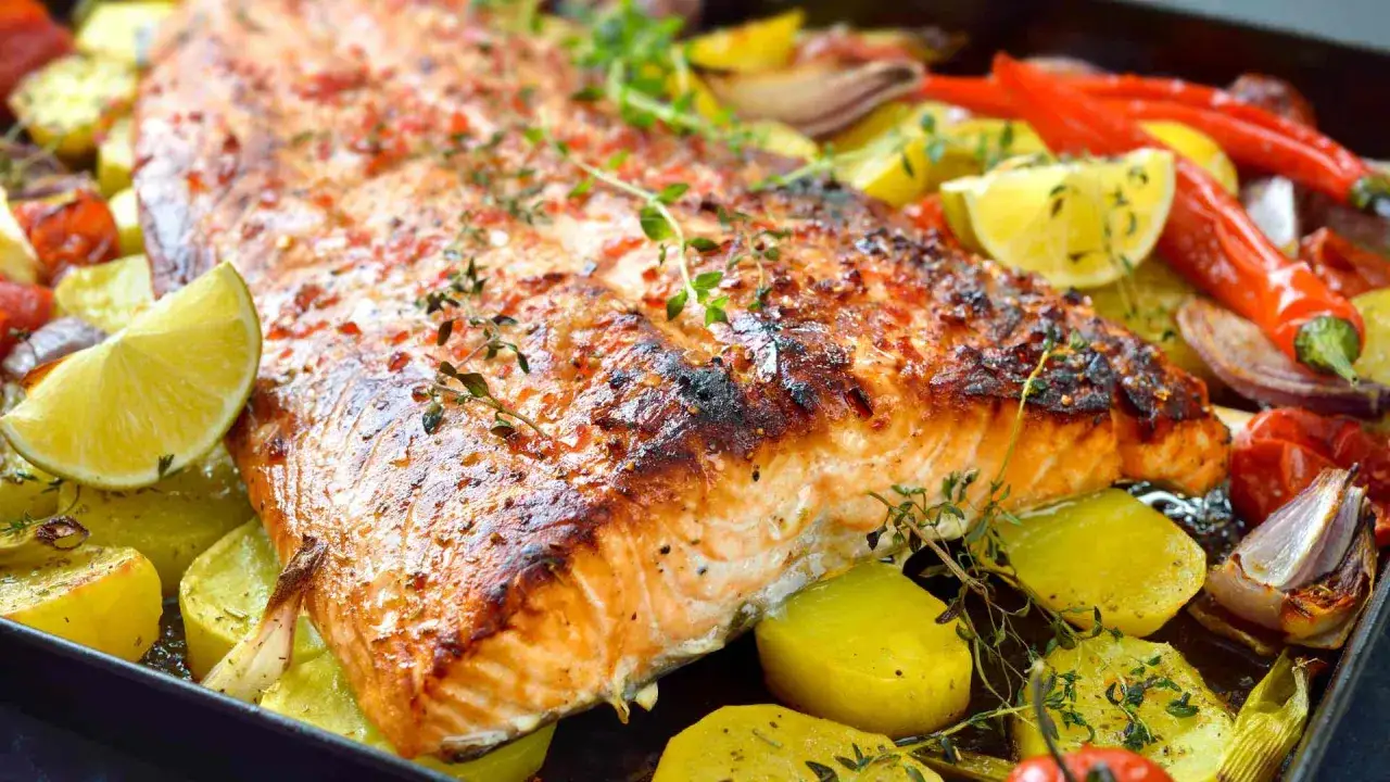 Un plat appétissant de saumon au four avec pommes de terre, citrons, oignons et piments. Quel vin avec du saumon au four ? Un blanc sec ou un rosé léger serait parfait.