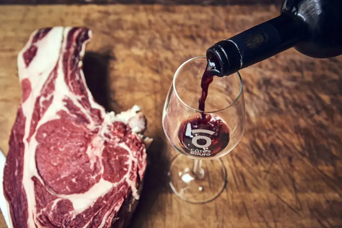 Un verre de vin rouge est versé à côté d'une côte de bœuf crue sur une planche en bois. Un accord parfait pour un repas gourmand.