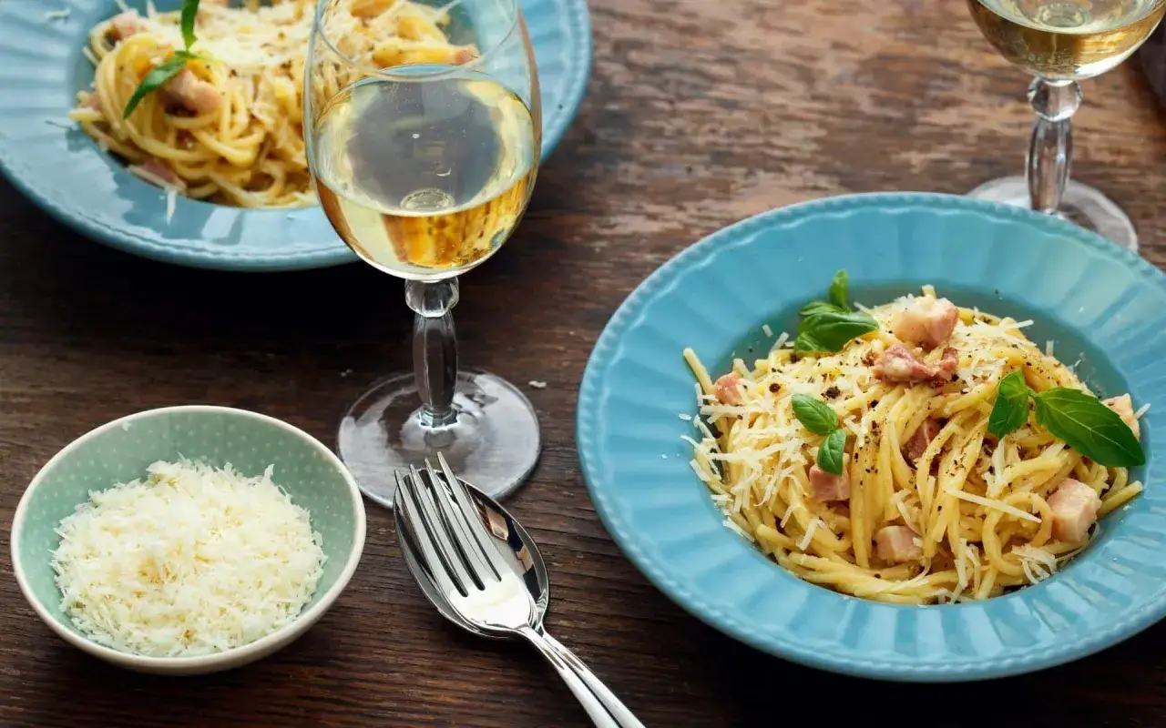 Un délicieux vin blanc accompagne un plat de spaghetti carbonara, garni de parmesan râpé et de basilic frais.