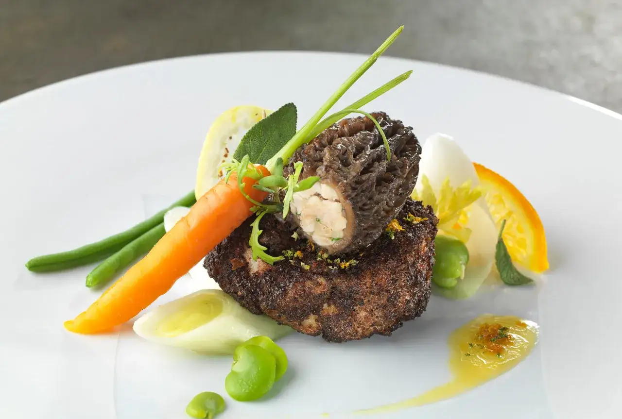 Quel accompagnement avec des ris de veau aux morilles ? Ce plat présente un ris de veau, une morille farcie, des haricots verts, une carotte, des fèves, du poireau et une tranche d'orange.