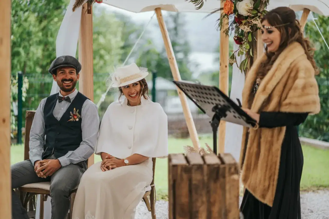 Un couple rayonnant lors d'un mariage style Peaky Blinders. L'homme porte une casquette et un gilet, la femme un chapeau chic.