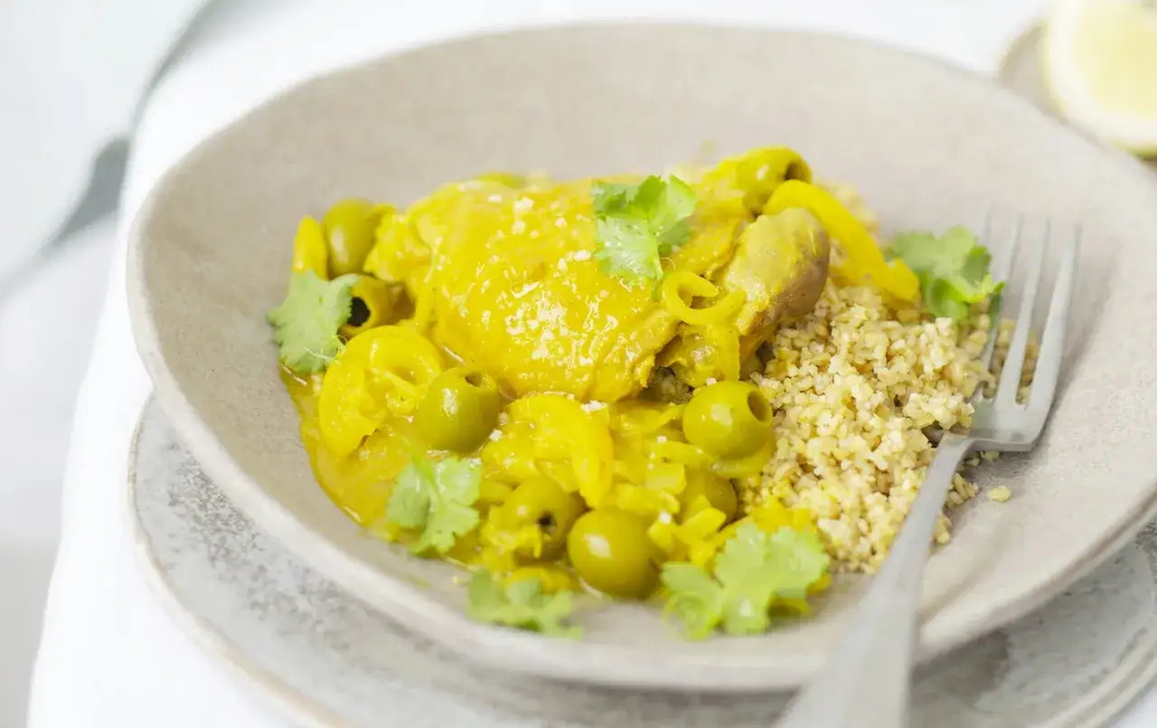 Un plat de vin avec tajine poulet citron, olives vertes et coriandre fraîche, servi avec du boulgour.