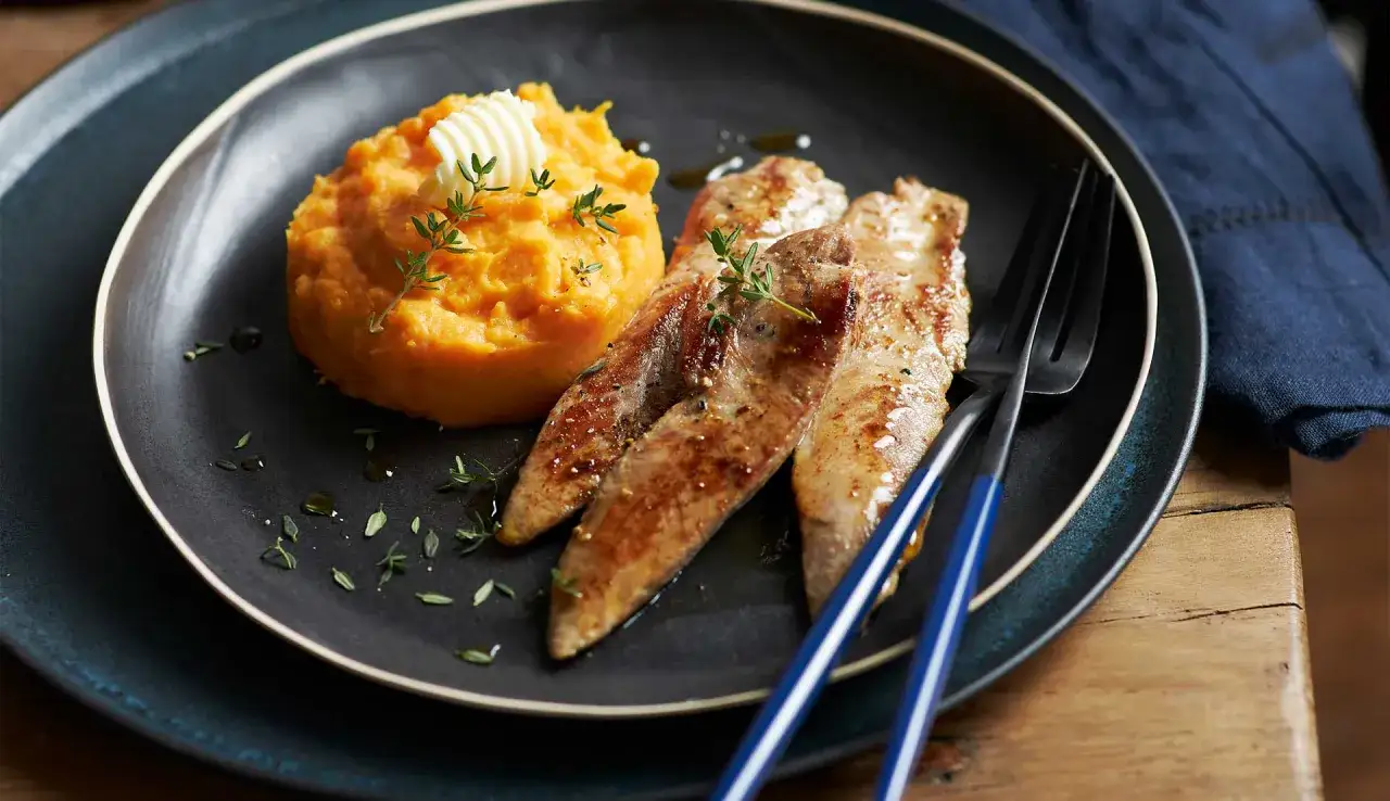 Quel accompagnement avec des aiguillettes de canard ? Une pur&eacute;e de patates douces onctueuse, garnie de beurre et de thym frais, sur une assiette sombre.