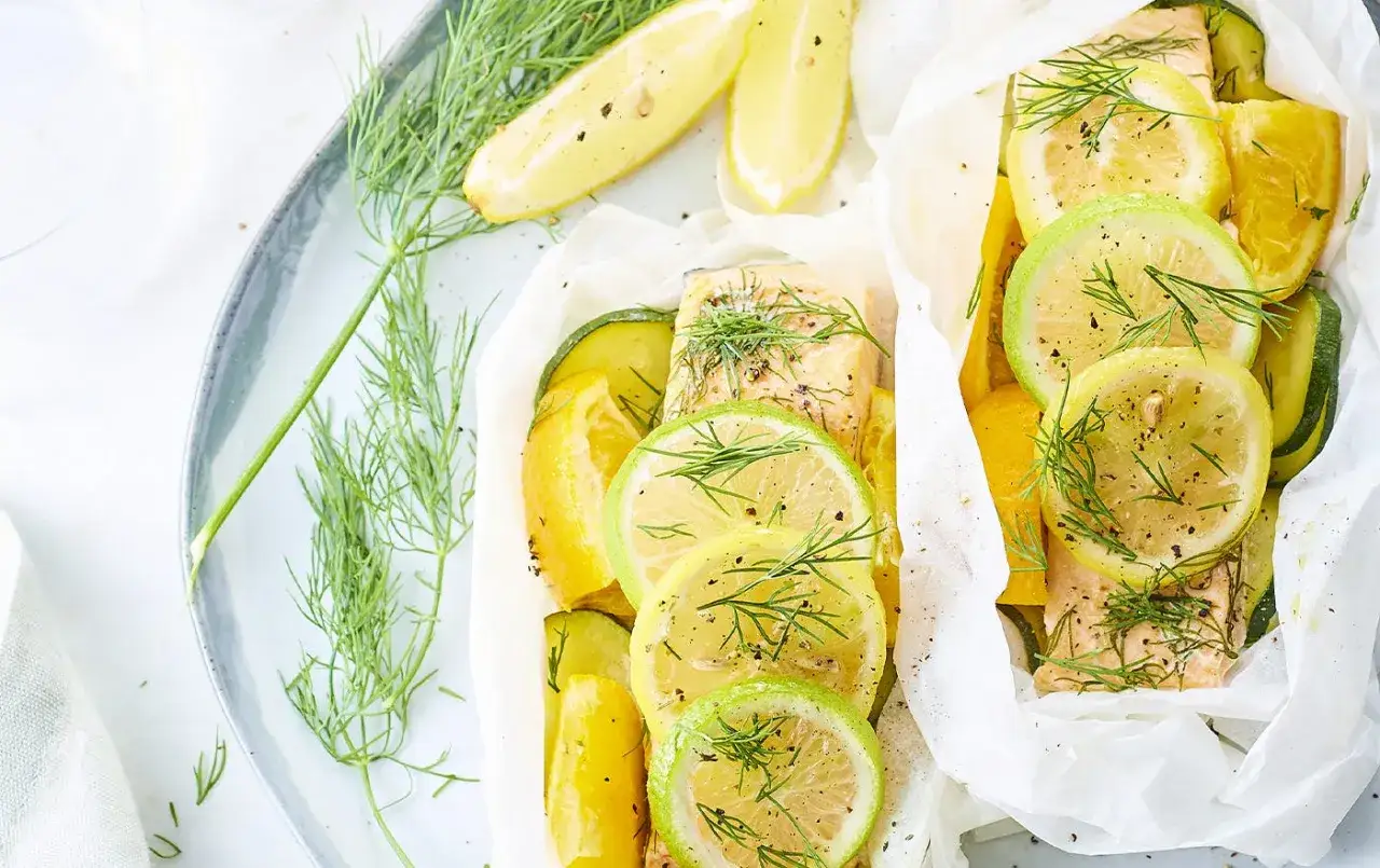 Deux papillotes de saumon aux agrumes et courgettes, parsemées d'aneth. Idéal pour savoir quel vin avec du saumon en papillote.