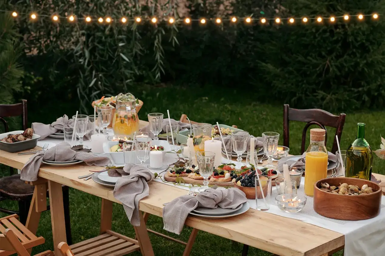 Table dress&eacute;e pour un brunch mariage en ext&eacute;rieur, ambiance chaleureuse avec guirlandes lumineuses et bougies.
