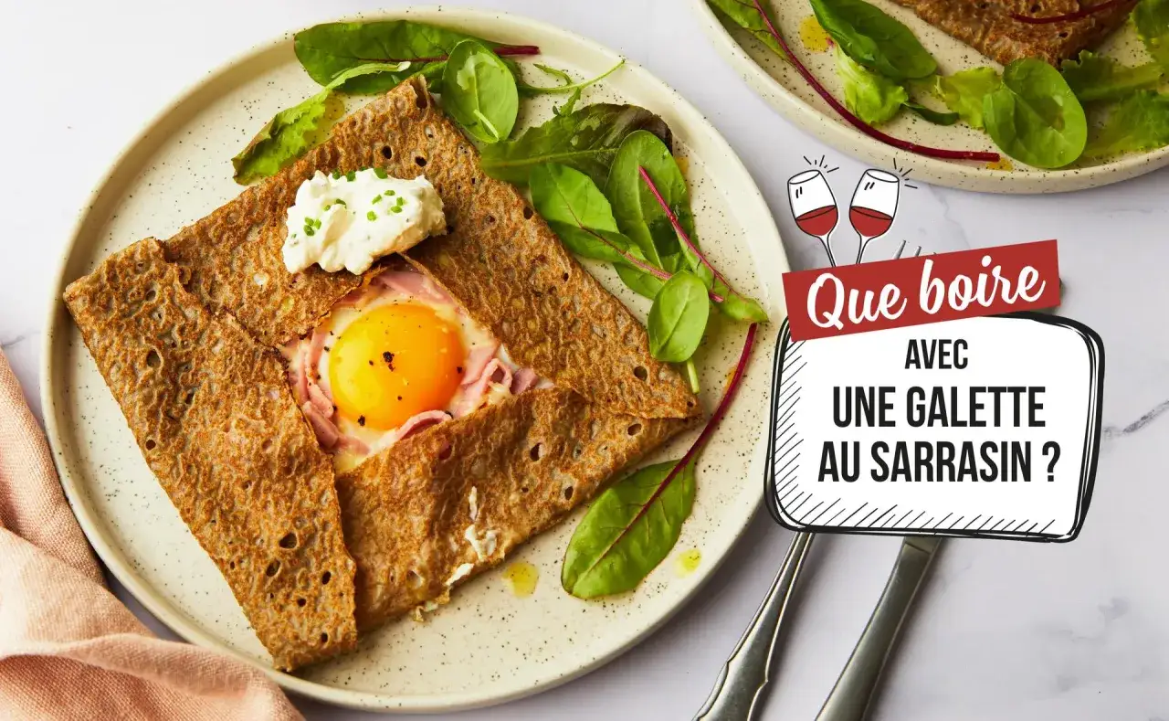 Une galette au sarrasin garnie d'un œuf et de jambon, servie avec de la crème et de la salade. Un verre de vin rouge suggéré pour accompagner.