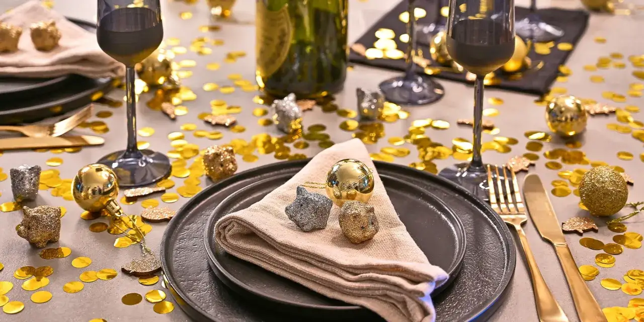 Table dressée pour le Nouvel An, paillettes dorées et argentées, boules festives, verres à pied, couverts dorés. Une belle idée buffet nouvel an.