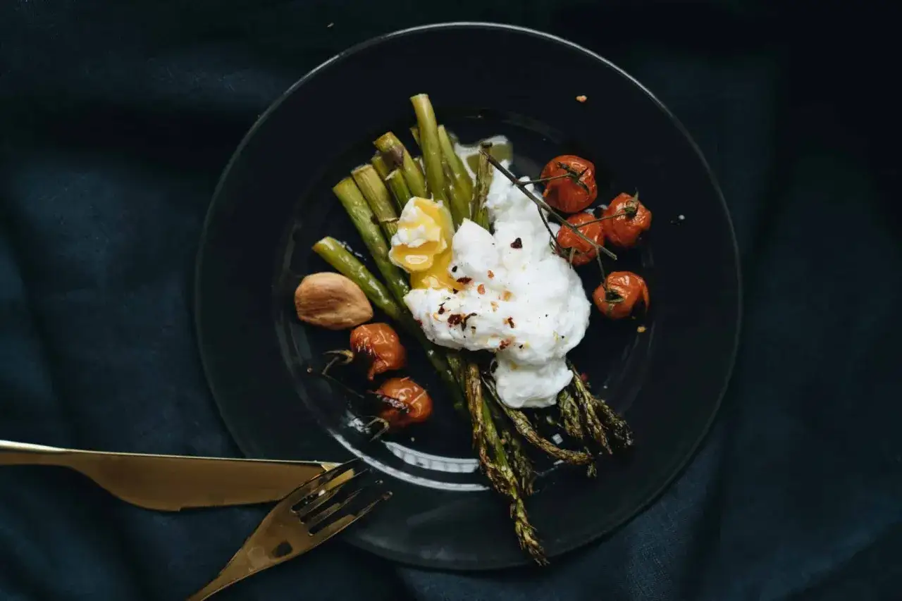 Asperges poêlées, œuf poché et tomates cerises sur une assiette noire. Un plat qui invite à se demander quel vin avec asperges.