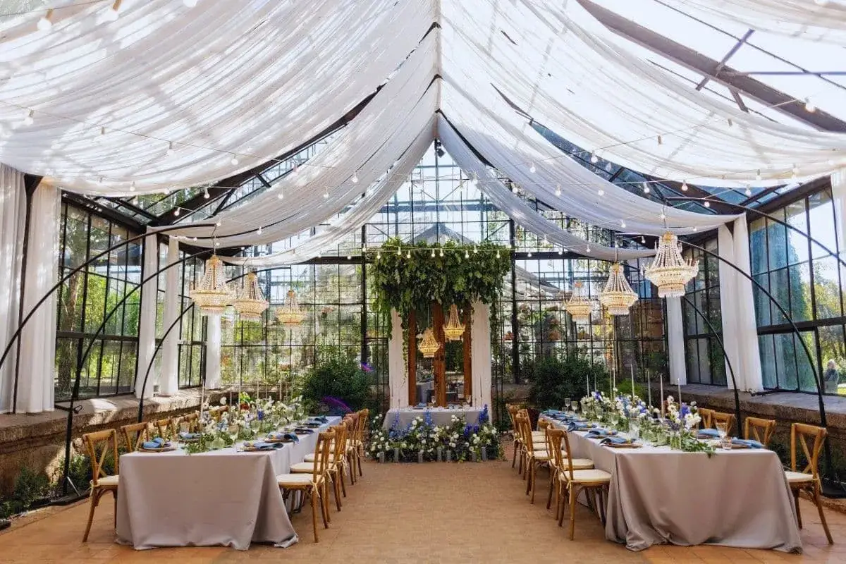 Magnifique serre am&eacute;nag&eacute;e pour un mariage de 50 personnes, avec des tables dress&eacute;es, des lustres &eacute;tincelants et une d&eacute;coration florale luxuriante.