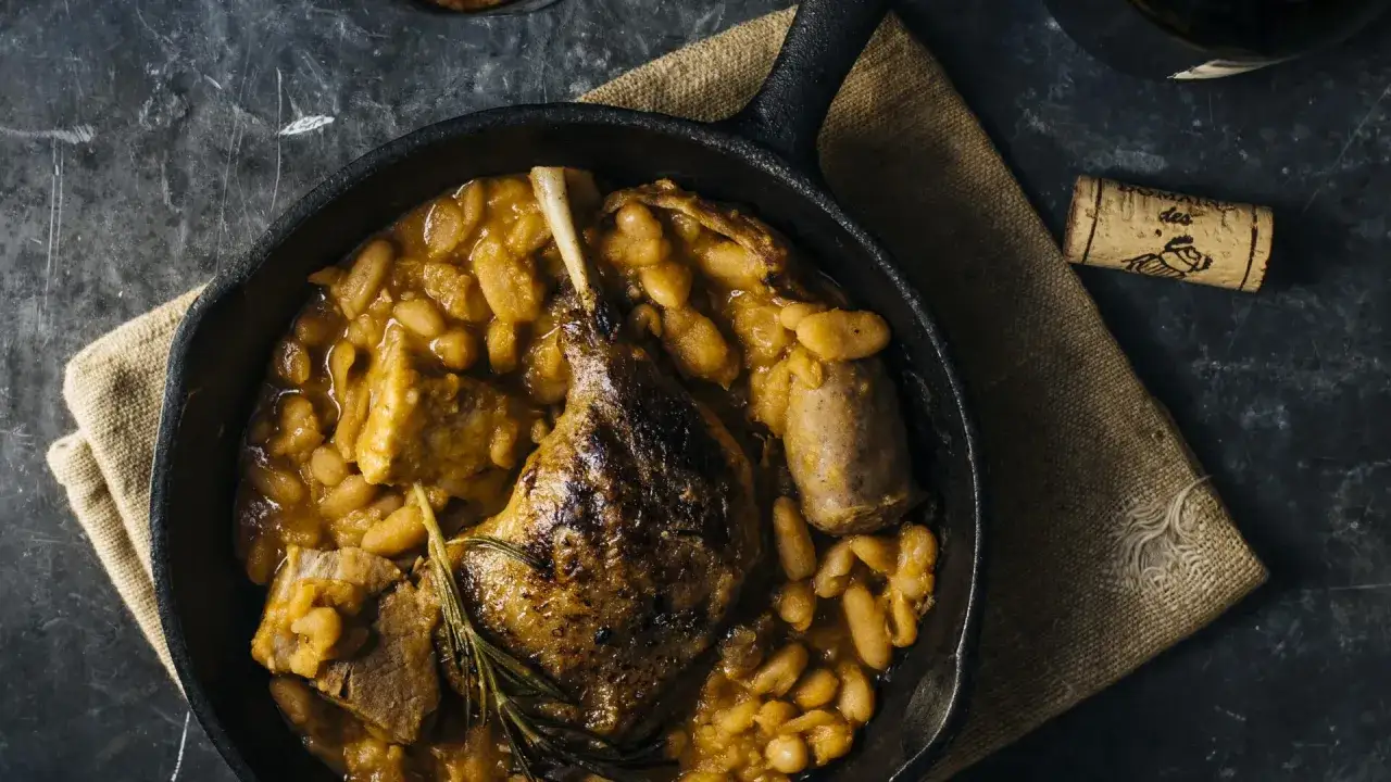 Un plat de cassoulet mijoté dans une poêle en fonte, accompagné d'un bouchon de vin de Bordeaux.