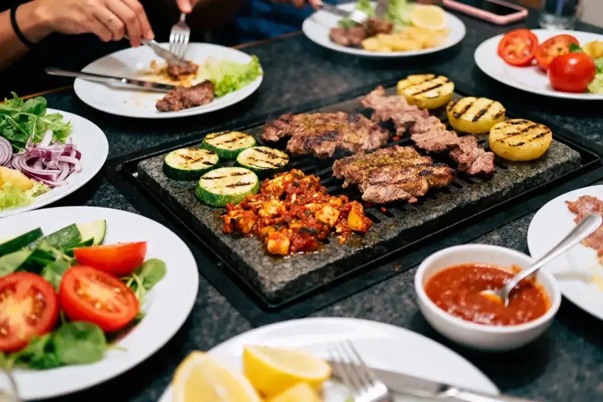Viande grillée sur pierre chaude, courgettes, tomates et salades. Un repas convivial, parfait pour savoir quel vin avec une pierrade.