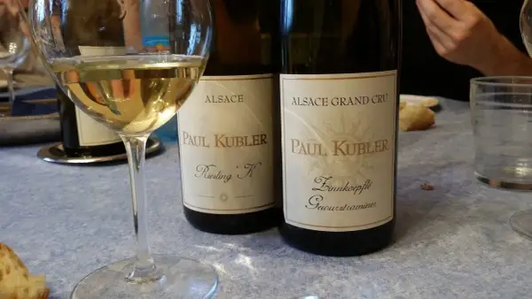 Verre de vin blanc alsacien, idéal pour accompagner une choucroute. Deux bouteilles Paul Kubler Riesling K et Gewurztraminer sont visibles.