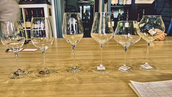 Six verres à vin vides alignés sur un comptoir de bar en bois, prêts pour une dégustation.