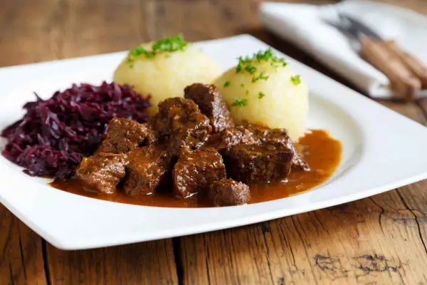 Un plat appétissant de daube de sanglier au vin blanc, servi avec des quenelles et du chou rouge.