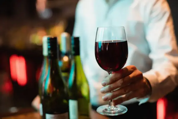 Main tenant d'un verre de bon beaujolais, avec des bouteilles en arrière-plan.