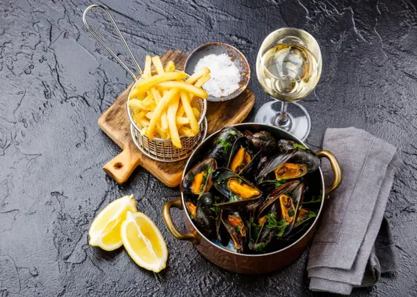 Un plat de moules frites, accompagné de quartiers de citron, d'une coupelle de gros sel et d'un verre de vin blanc.
