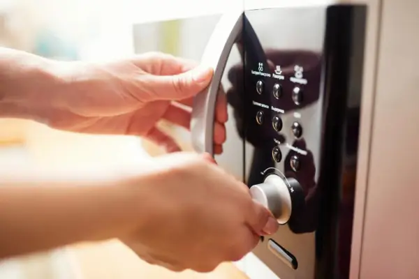 Mains de femme ouvrant un micro-ondes en inox. Elle tourne le bouton pour régler le temps de cuisson.